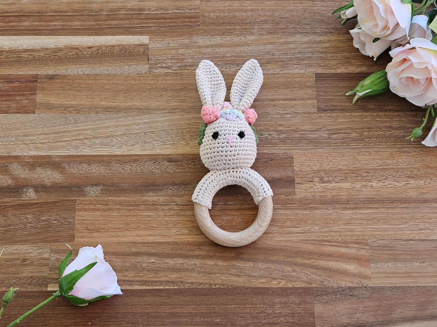 Crocheted bunny teething ring on a wooden surface with flowers.