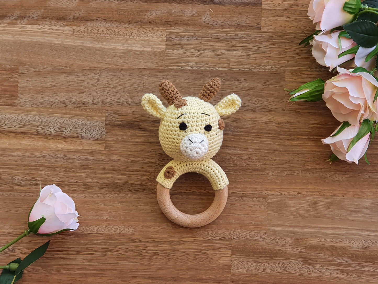 A crocheted giraffe baby teething ring toy with a wooden ring.