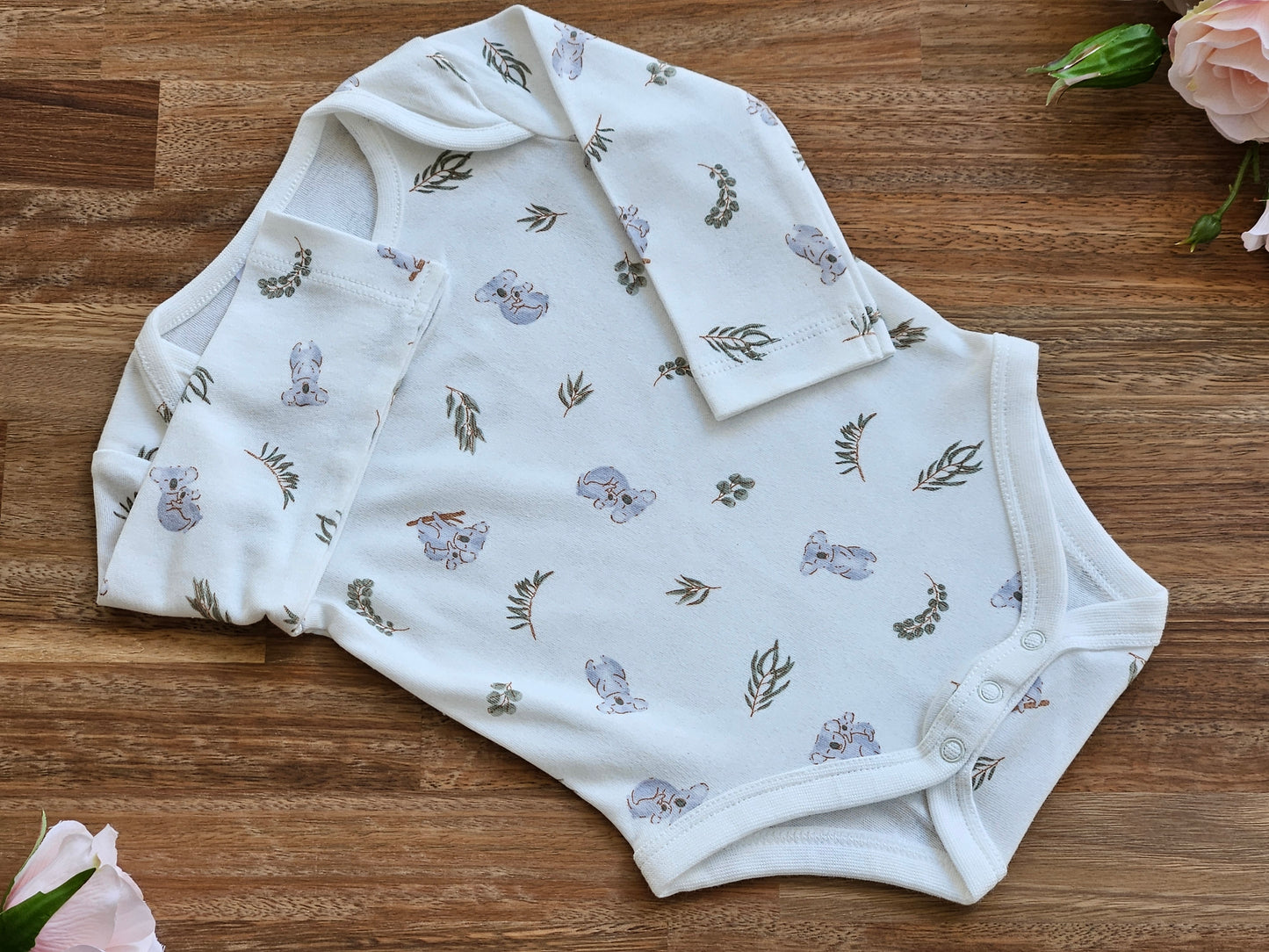 A cream long-sleeve baby bodysuit with a delicate print of grey koalas and green leaves.