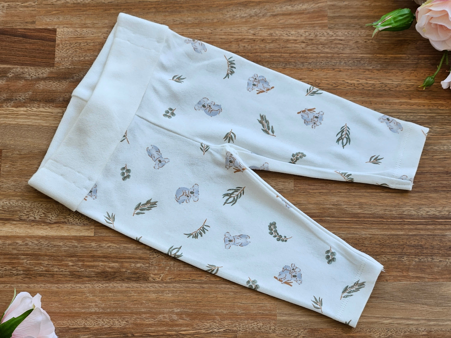 A cream coloured baby leggings  with a delicate print of grey koalas and green leaves rolled waistband.