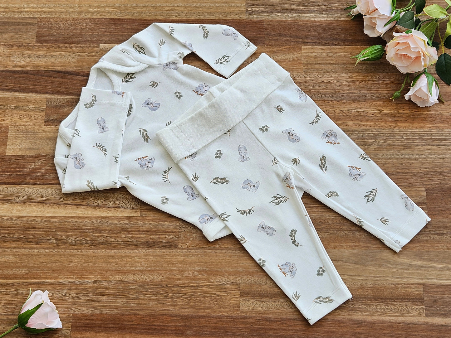 A cream long-sleeve baby bodysuit with a delicate print of grey koalas and green leaves with matching leggings.