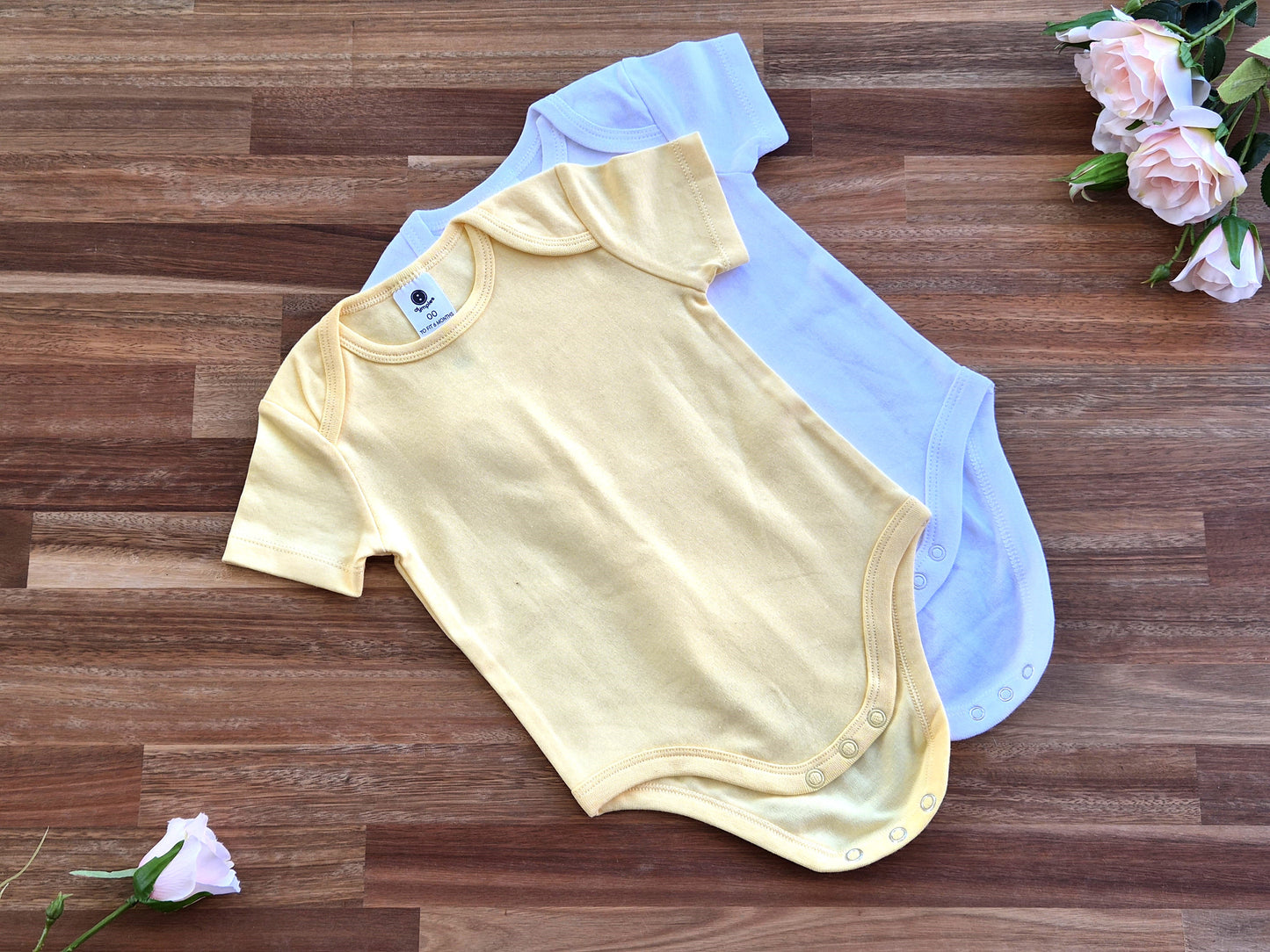Two short-sleeve baby rompers, one pale yellow in front and one light blue behind it.
