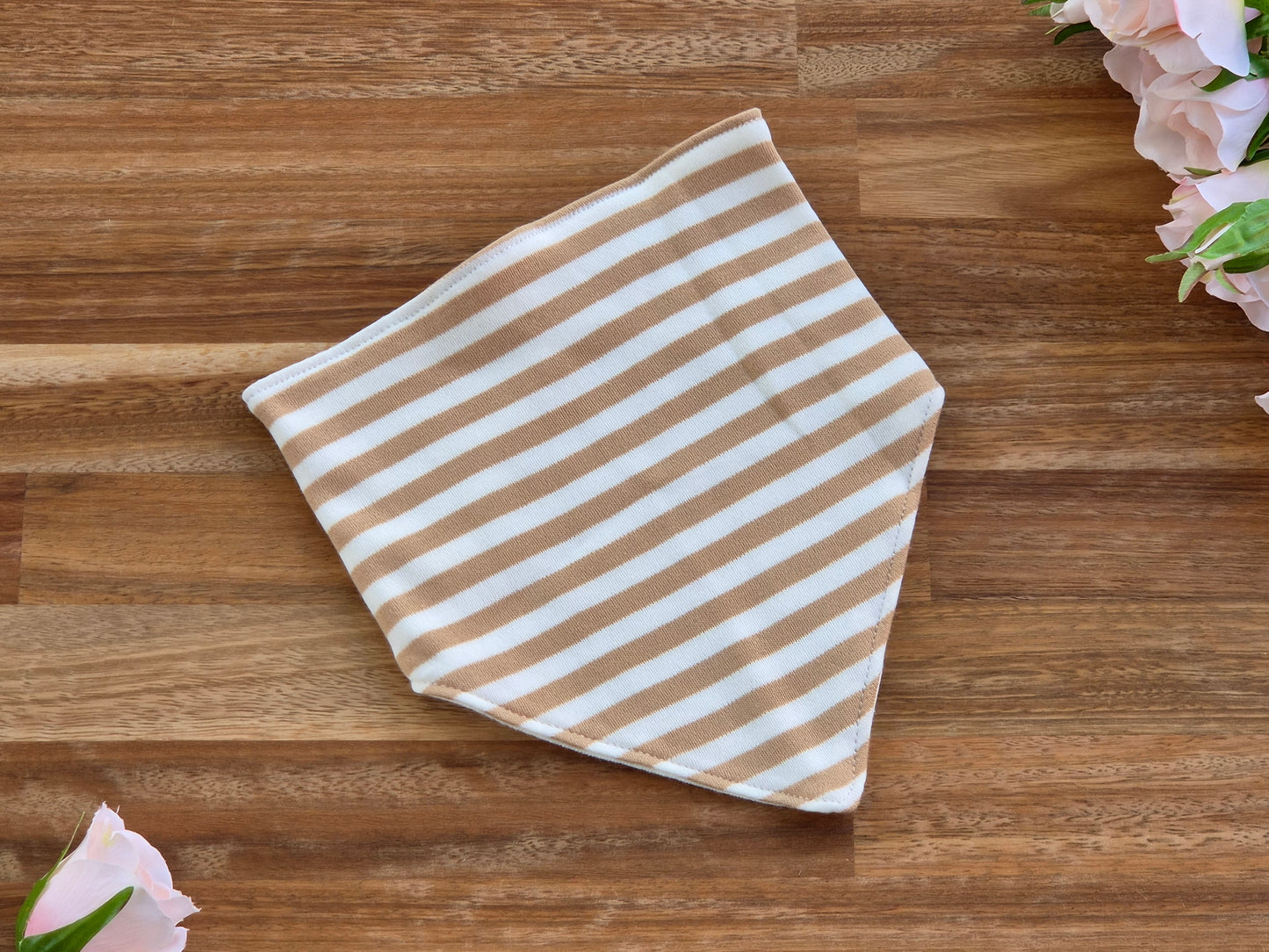 A square bandana with horizontal tan and white stripes, laid flat on a brown wooden surface with pink flowers in the corners.