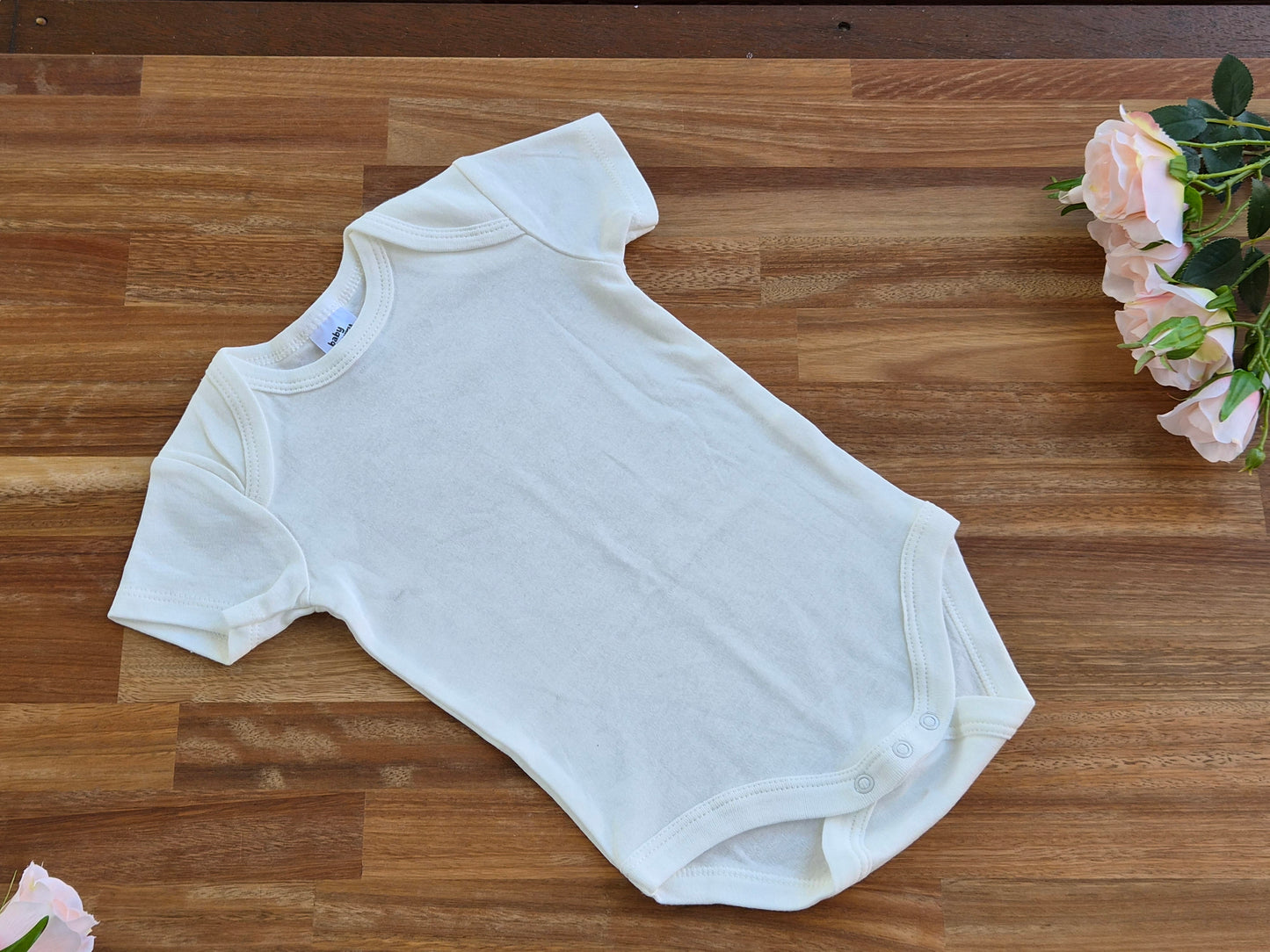A plain white short-sleeve baby bodysuit laid flat on a wooden surface.